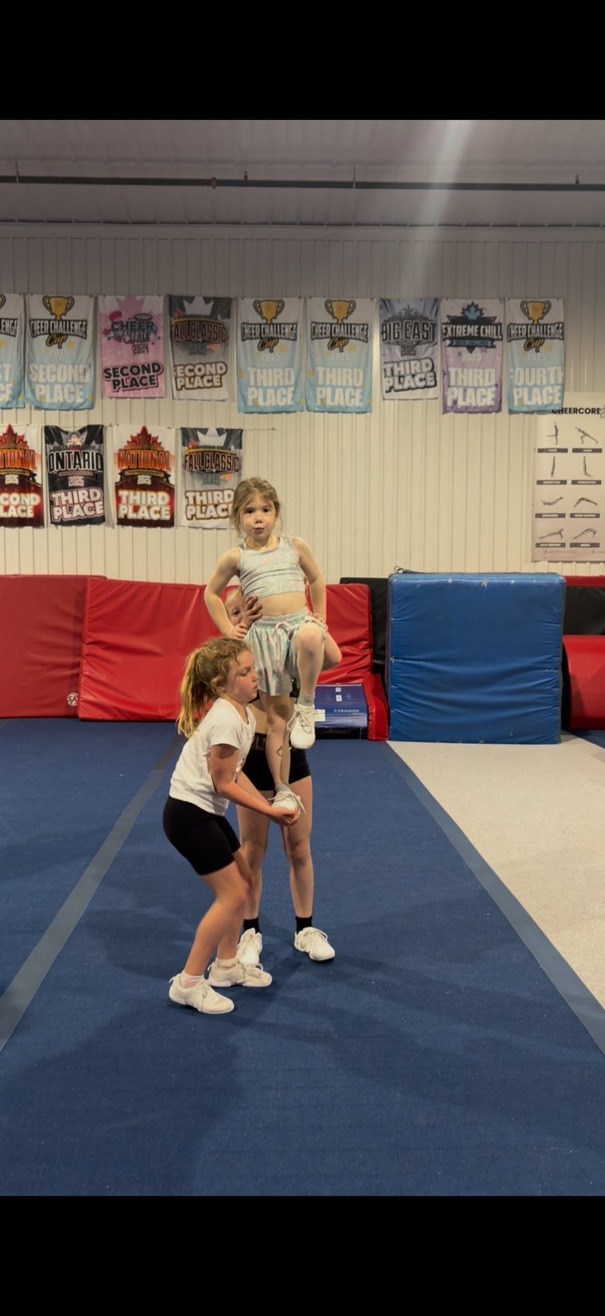 Two young CheerCore Jags athletes practising a shoulder stunt in the gym