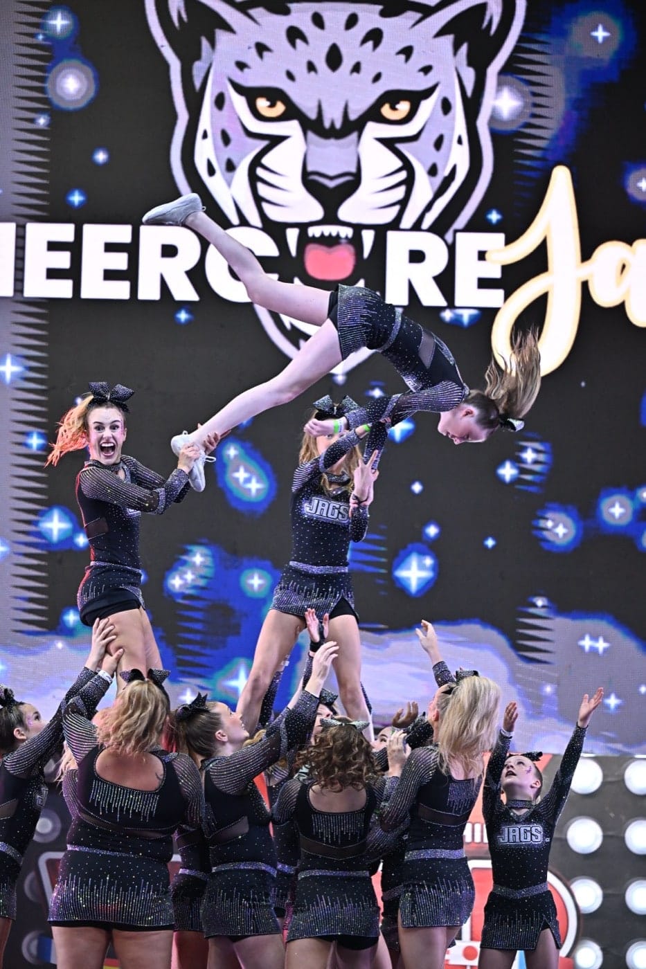 Elite Cheer athletes performing a stunt on stage under the CheerCore Jaguar backdrop