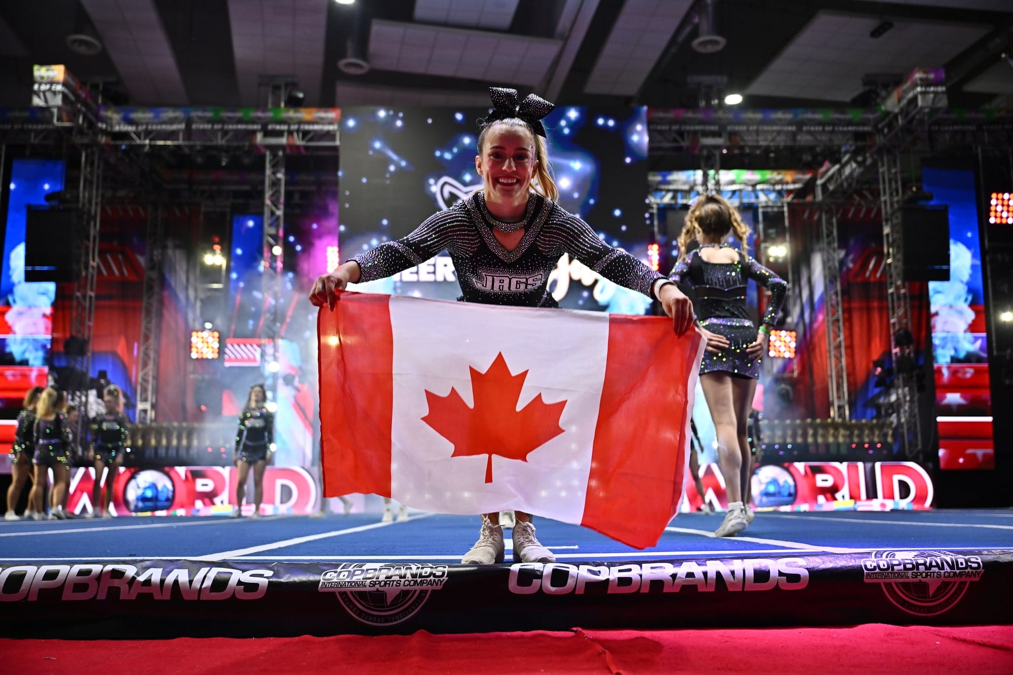 A CheerCore Jags Elite athlete holding the Canadian flag on the competition floor at Worlds