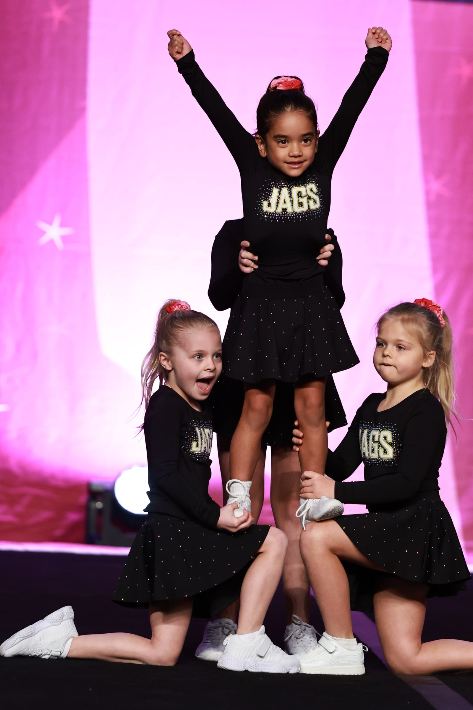 Three Novice Cheer athletes hitting a stunt, the flyer with both arms raised